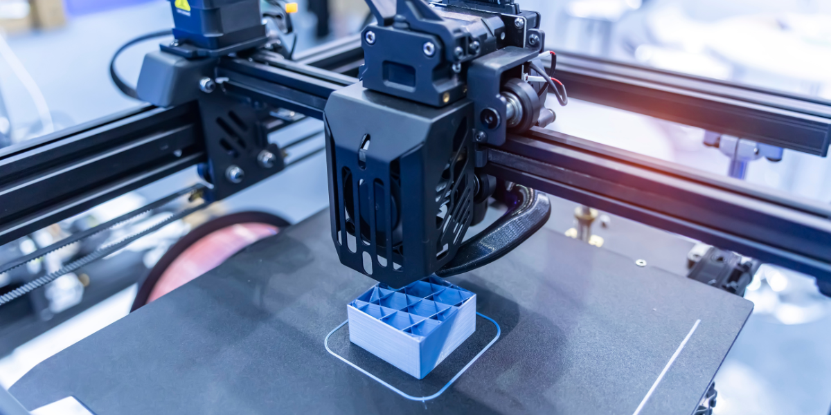 3D printer creating blue geometric object on build platform in makerspace