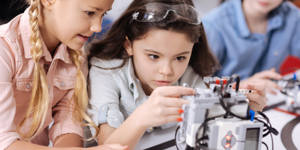 Two young girls working together on robotics engineering project with electronic components, demonstrating collaborative STEM learning and problem-solving skills