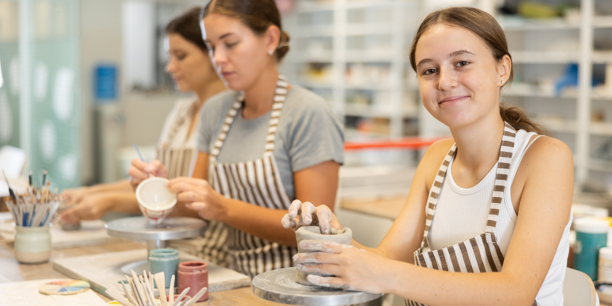 Teenage students work with clay on pottery wheels in a well-equipped art studio, showcasing the advanced creative skills and collaborative learning that occurs when schools teach art in schools programs.