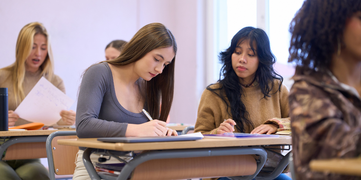 Diverse group of teenagers focused on writing exam papers in classroom, showcasing concentration techniques and study skills that help teens concentrate during important academic assessments.