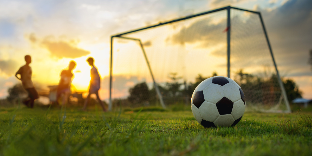 Children playing soccer on grass field with goalposts at sunset
