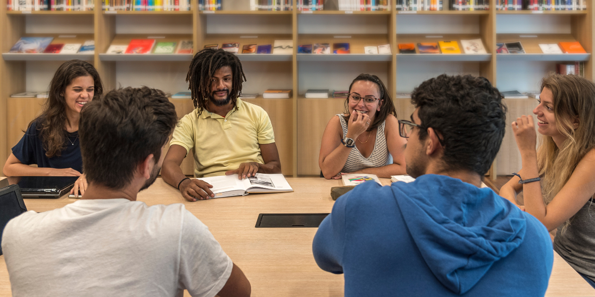 Diverse group of students debating in library setting with books in background