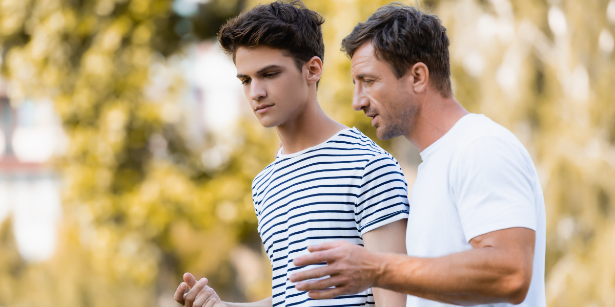 Father having calm, supportive conversation with teenage son outdoors, showing positive parent-child communication and conflict resolution modeling