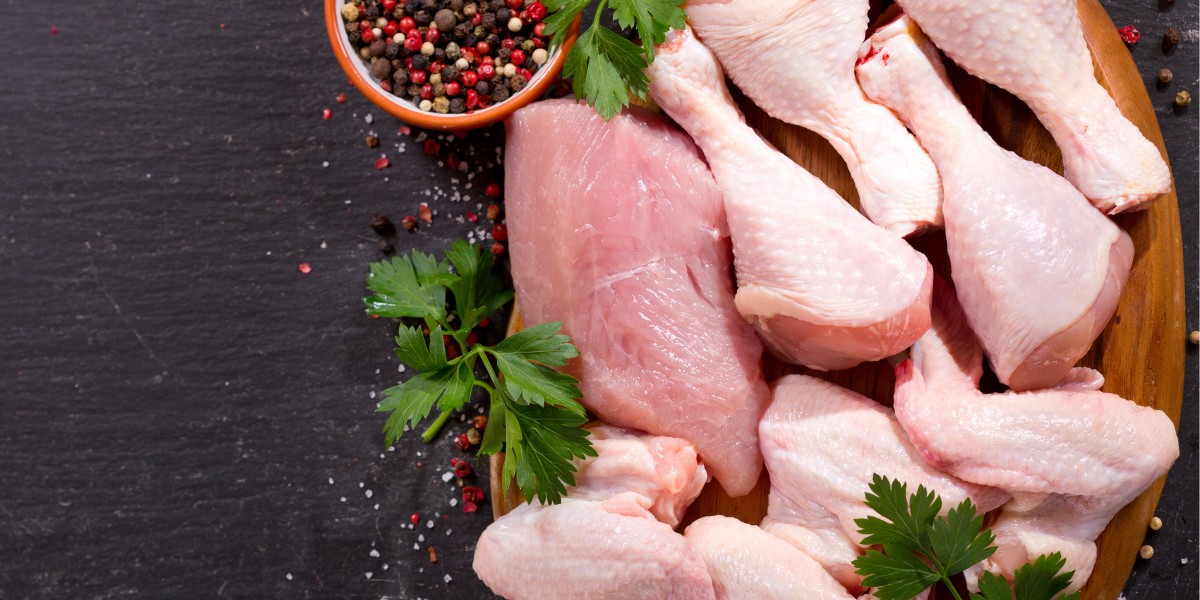 Assorted raw chicken pieces including breasts, thighs, drumsticks and wings arranged on wooden cutting board with herbs and peppercorns, illustrating muscle biology concepts