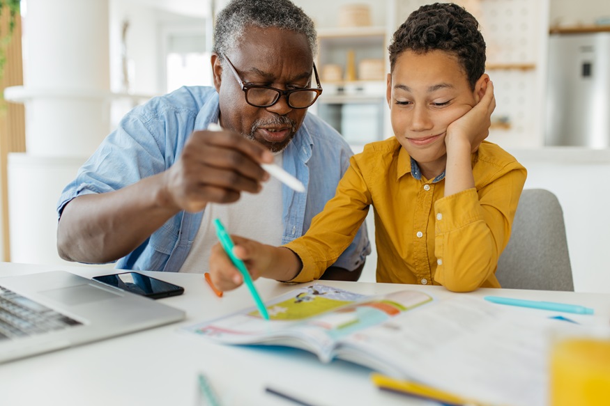 Grandfather tutoring his grandson at home. The child is patiently listening and learning while grandad showing him how to solve the problem.