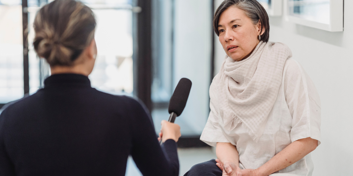 Student practicing interview skills with teacher, holding microphone while learning about newsworthy story elements for student newspaper