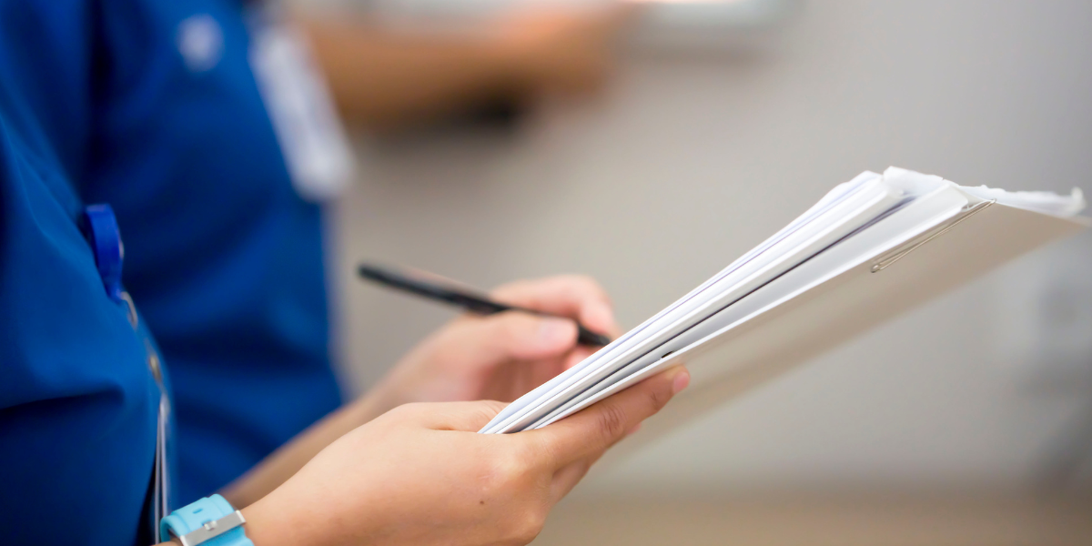 Student in blue shirt holding white notebook and pen while researching newsworthy story elements for student newspaper