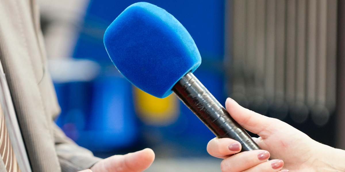 Hand holding blue microphone for student newspaper interview to identify newsworthy story elements