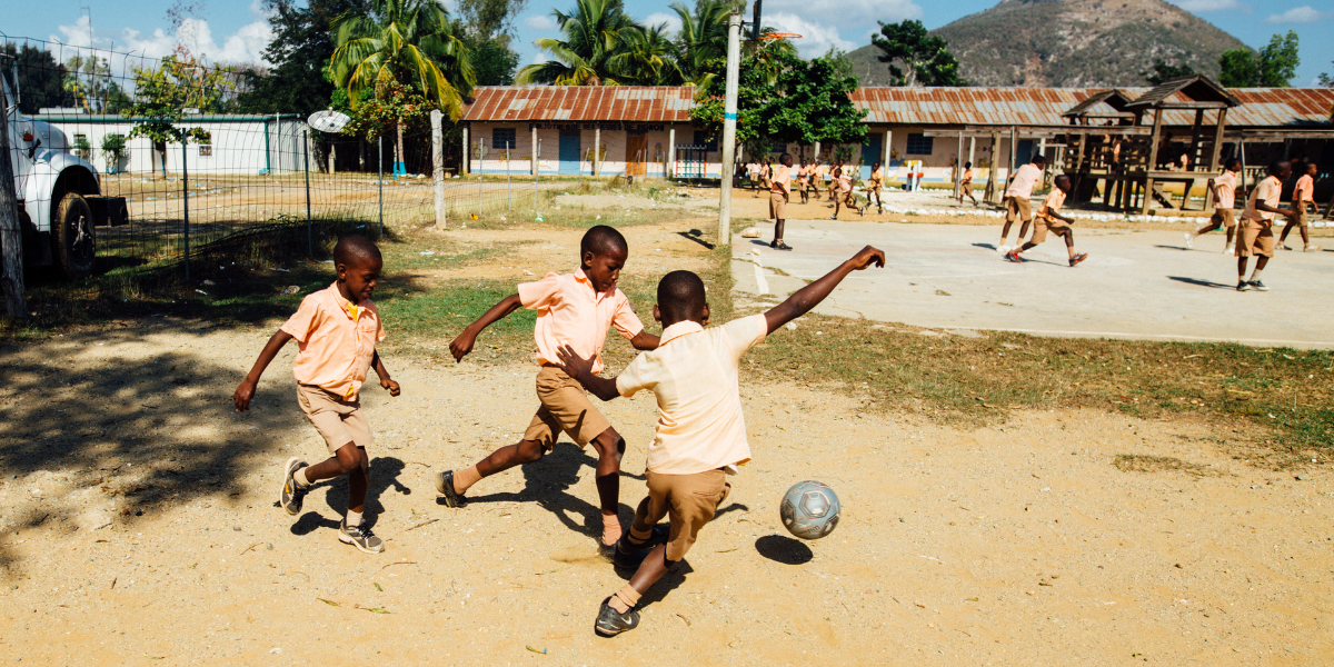Children playing soccer with basic equipment in schoolyard showing resource differences